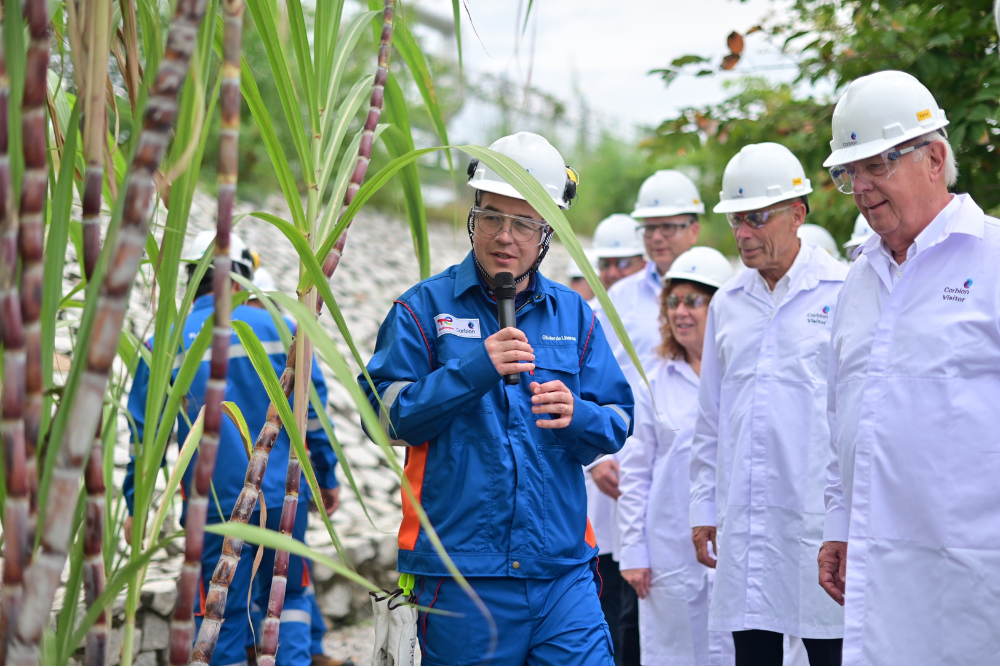 Man speaking in to crowd in front of sugarcane